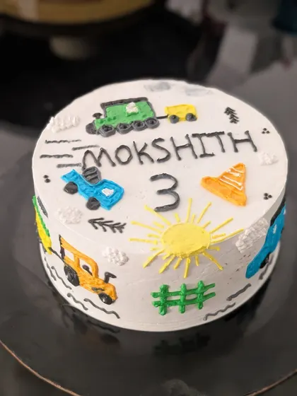 A charming, hand-drawn style cake featuring various vehicles. This buttercream cake is decorated with a train, cars, and a bulldozer for a 3rd birthday.