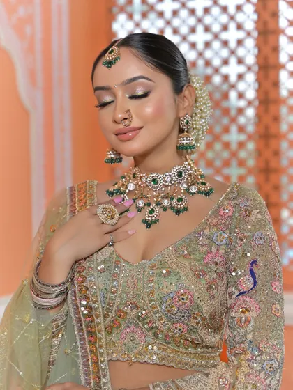 A serene and classic bridal portrait. The bride's eyes are closed, drawing all attention to the flawless makeup and the magnificent Polki and emerald jewellery set.