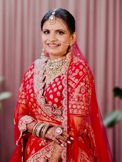 A full-length portrait of the bride in a classic red lehenga. The makeup is balanced to look beautiful in both close-up and full-length photos.