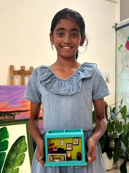 A young artist proudly holding the miniature room she created in a shadow box workshop.