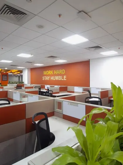 We used biophilic design principles in this workstation area, incorporating lush green planters to separate spaces and improve ambiance. The "Work Hard Stay Humble" wall graphic reinforces company values within the daily workspace.