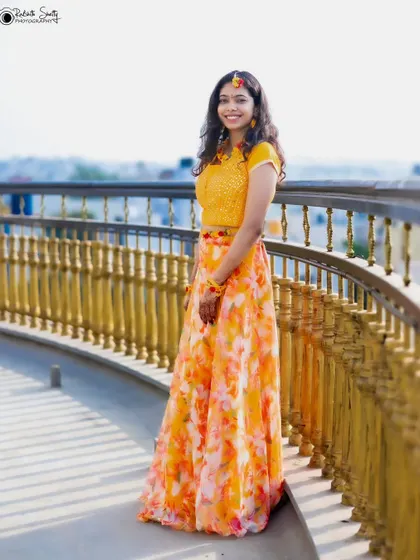 A beautiful full-length portrait of the bride on her Haldi day. Her floral-patterned lehenga and the sunny outdoor setting create a fresh and joyful look.