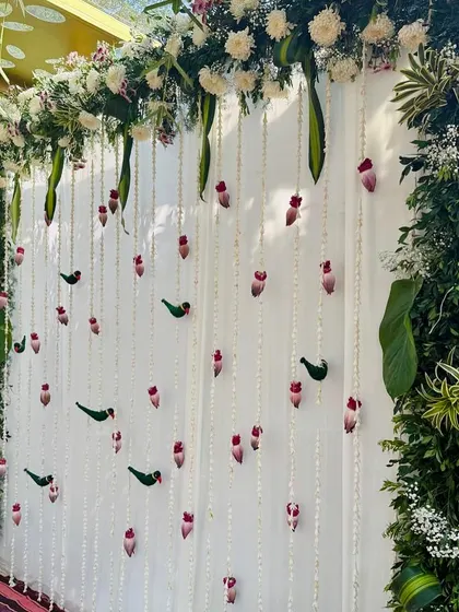 A detailed view of the Varapooje backdrop, showing the delicate parrot and lotus bud hangings made from flowers and leaves.