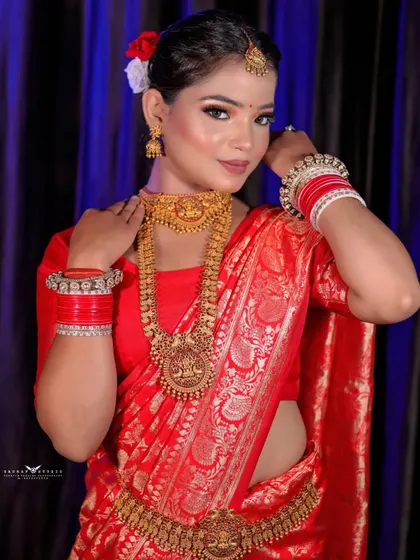 A beautiful portrait of a bride in a traditional Bengali red saree and gold temple jewellery. Her pose is graceful and highlights the rich cultural attire.