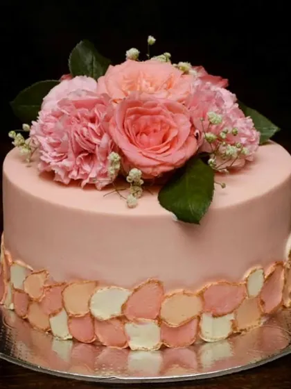 A beautiful cake in a pretty peach color palette. The bottom edge is decorated with a hand-painted petal effect, and the top is crowned with fresh pink carnations and roses.