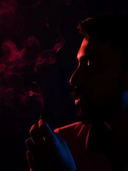 A moody and atmospheric portrait using low-key lighting. The combination of red and blue light with smoke creates a cinematic feel, sculpting the subject's profile against the dark background.