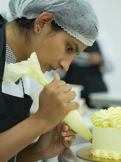 A student in deep concentration, piping perfect yellow rosettes onto a cake. We teach various nozzle techniques so you can create a wide array of beautiful patterns with buttercream.