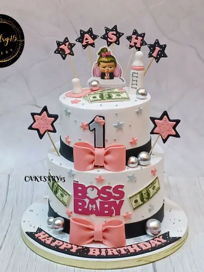 A stylish two-tier "Lady Boss" themed cake for a first birthday. This design uses a pink, black, and white color scheme with cute bows and star accents.