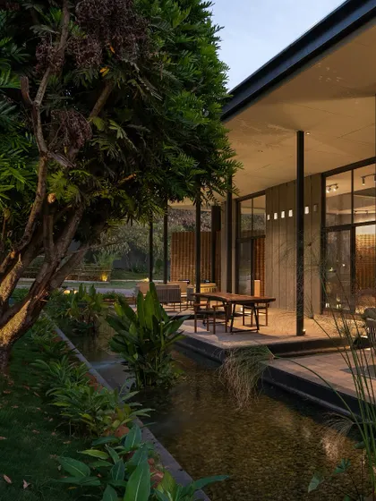 A tranquil water channel runs alongside the building's veranda, reflecting the sky and surrounding plants. This water feature not only adds a sensory element but also helps to passively cool the immediate area.