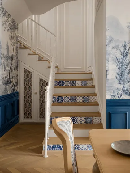 This staircase, adjacent to the dining area, features custom-painted tile risers that echo the blue-and-white theme of the room. The deep indigo wainscoting adds a bold contrast to the natural wood floors.