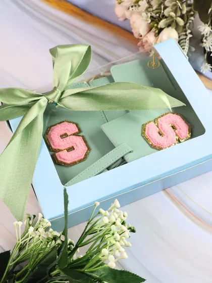 A soft and elegant travel combo for Rakhi, featuring mint green accessories with pink monograms, all tied up with a beautiful green ribbon.