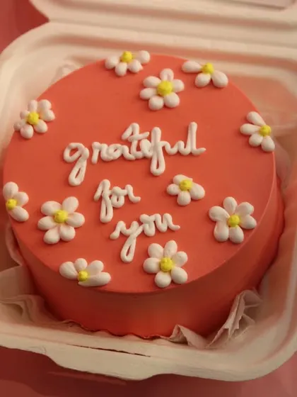 A lovely coral-colored bento cake with the message "grateful for you" and decorated with small daisies. A sweet way to show appreciation.