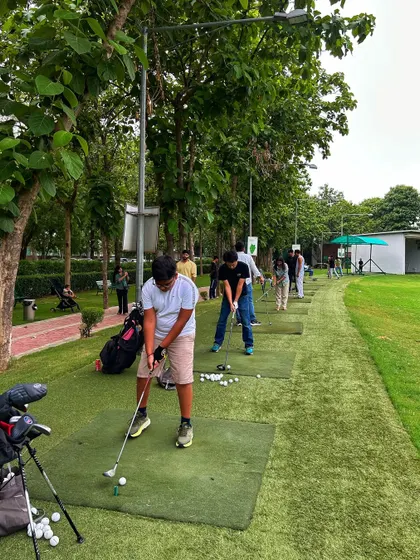 A golfer in the foreground prepares to swing, with a full line of players visible down the range.