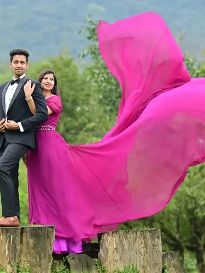 A dramatic pre-wedding shoot in a beautiful outdoor location. The bride-to-be is wearing a magenta gown with a very long trail, coordinated with his classic black suit.