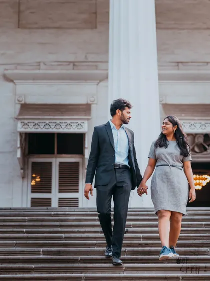 A full-length shot of the couple holding hands while walking down grand steps, blending a casual style with an elegant location.