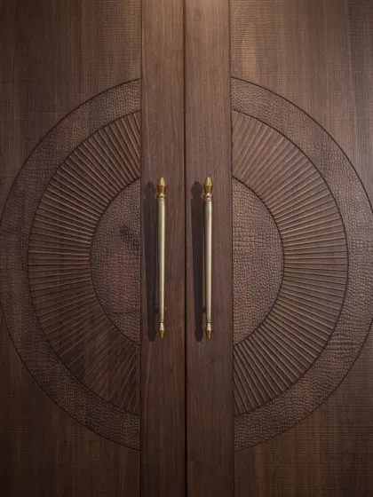 A close-up of the intricately carved double door, highlighting the different textures and the elegant brass handles.