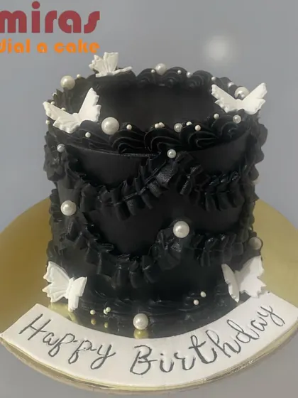 A dramatic and elegant black buttercream cake. The design features intricate black ruffles, delicate white butterflies, and pearls, offering a sophisticated and moody aesthetic.