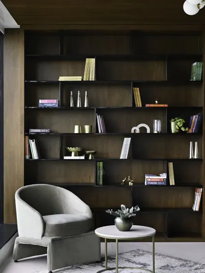 A reading nook with a view. The dark, full-height bookshelf creates a dramatic, library-like feel, while the comfortable armchair is perfectly positioned to take advantage of the natural light from the large window.