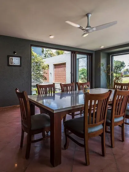 The formal dining room continues the home's contemporary aesthetic with dark grey walls and large windows. The space is designed to feel connected to the outdoors, offering views of the surrounding greenery from every seat.