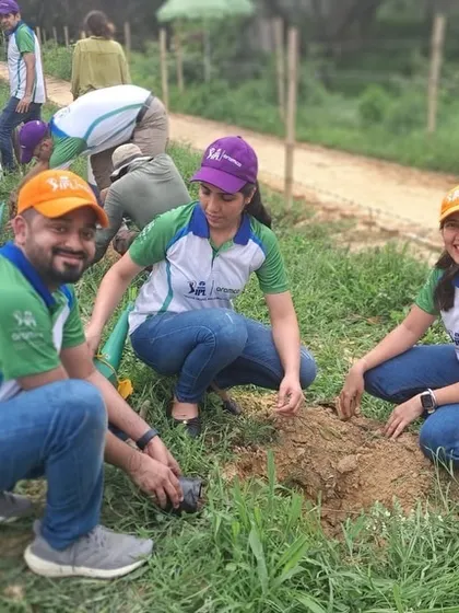 Three smiling volunteers from Aramco plant a native sapling together, contributing to the restoration of a vital water recharge zone.