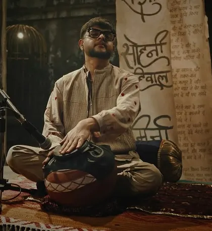 A shot of a musician from the 'Ishqbawla' set. The lighting is intimate and focused, using a single key light to highlight the artist and his instrument against a dark, textured background.