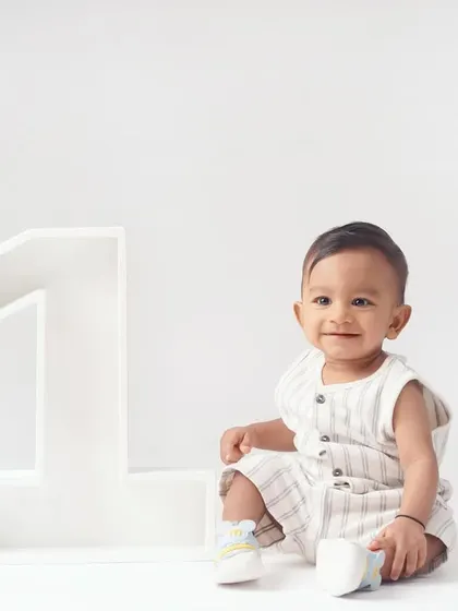 A happy baby boy in a striped romper smiles brightly while sitting next to a giant '1' for his minimalist first birthday shoot.