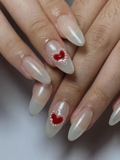 A simple yet stunning design. This features a sheer, milky white base on long almond nails, with a single, bold red heart made of tiny pearl beads.
