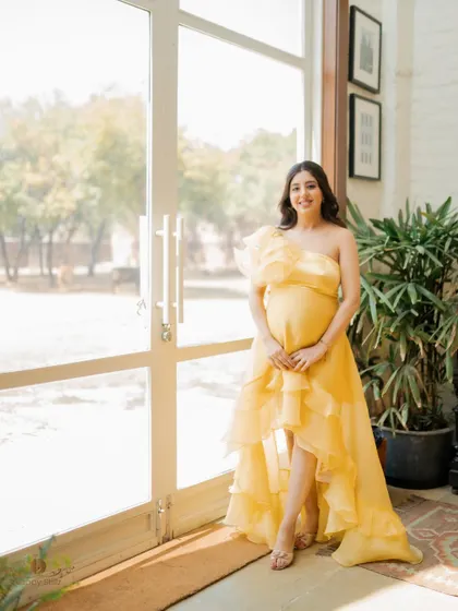 A bright and airy portrait of the mom-to-be standing by a large window, her yellow dress and happy smile bringing warmth to the photo.