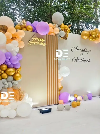 A stylish outdoor birthday setup with a modern backdrop and an organic balloon garland in pastel shades of lilac, peach, and gold.