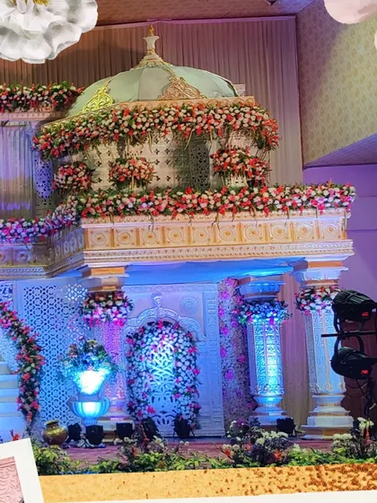 A magnificent multi-level stage designed to look like a floral palace. The structure features intricate carvings, a domed top, and a winding staircase, all lavishly decorated with flowers.