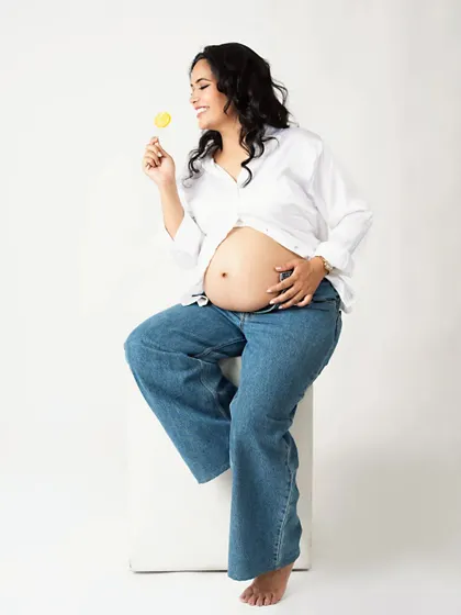 A sweet and playful solo shot. The mom-to-be enjoys a lollipop, adding a touch of fun and whimsy to her casual maternity portrait.