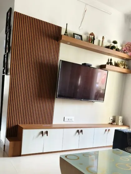 A simple yet elegant TV unit installation. The design incorporates a wooden louvered partition, a clean white console, and floating shelves for displaying decor.