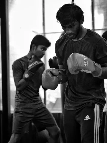 Two boxers work in unison, one on the bag and the other practicing shadow boxing. The entire gym is a place of constant learning and movement.