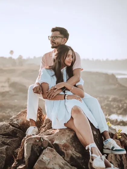A relaxed and intimate portrait of Harsh and Shreya sitting on the rocks by the sea, capturing a quiet moment during their beach pre-wedding shoot.