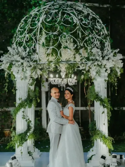 A fairytale moment for this couple, standing before a magnificent white gazebo adorned with flowers and greenery.