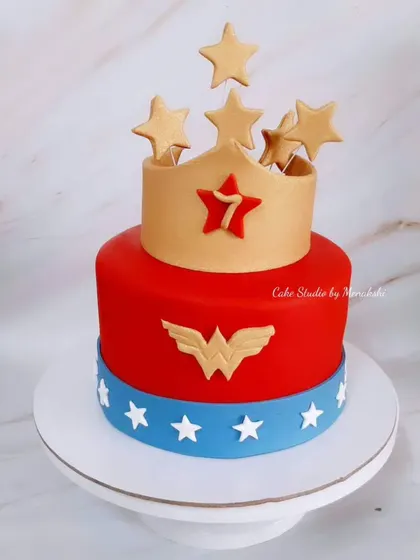 A powerful Wonder Woman themed cake for a 7th birthday. The design features the hero's classic red and blue colors, complete with her logo and a golden, star-studded crown.