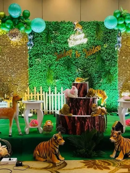 The cake-cutting area of the jungle party, with a tree-stump-themed cake stand surrounded by realistic animal figures.