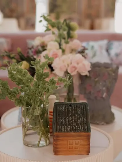 A close-up of a coffee table with a small floral arrangement and a quirky house-shaped ornament. These small, personal touches add charm and personality to the decor.
