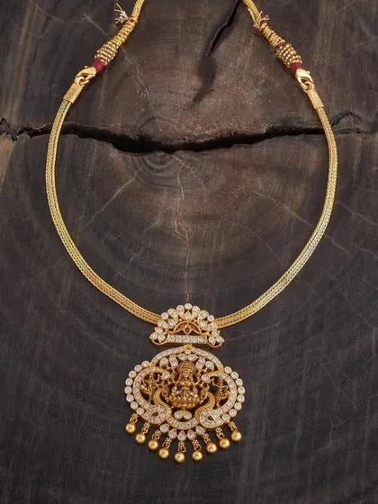 This elegant pendant necklace showcases a Goddess Lakshmi motif surrounded by sparkling white stones. The gold-toned pendant hangs from a sturdy, woven chain, making it a beautiful piece for both festive and daily wear.