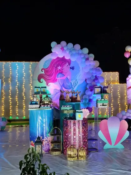 An outdoor mermaid theme setup at night, with fairy lights creating a magical underwater glow behind the main stage.