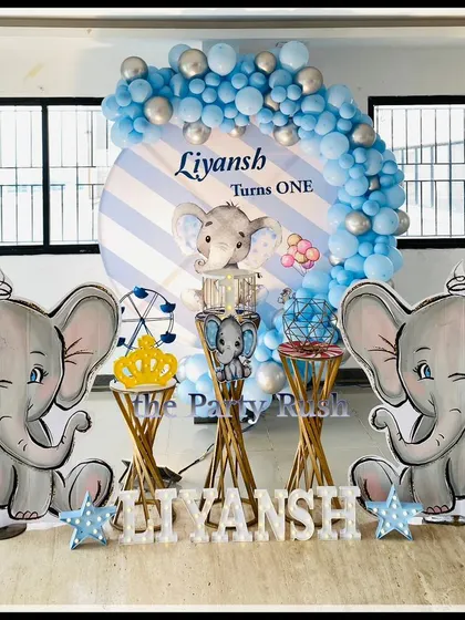 Liyansh's first birthday also featured the popular baby elephant theme. This setup includes two large elephant props, a striped blue and white backdrop, and star-shaped marquee lights for a touch of sparkle.