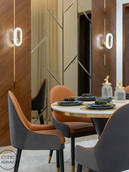 A close-up of a cozy dining nook. The round marble-topped table is paired with two-toned chairs in grey and tan leather. The wall features a combination of wood paneling and a custom-designed mirror that expands the space, while modern sconces provide soft, ambient light.