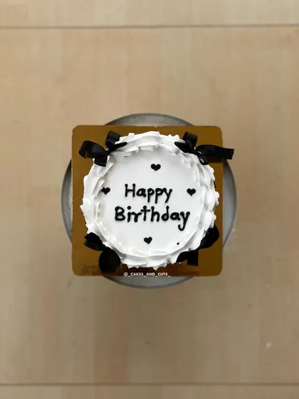 A top-down shot of the birthday cake with black bows, showing the clean piping work.