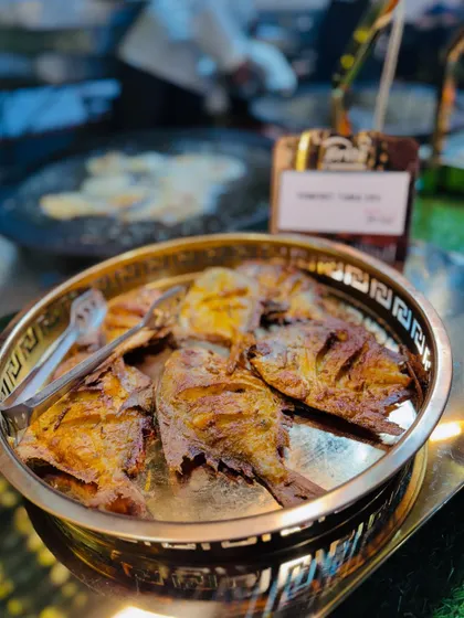 Freshly fried Pomfret served on a decorative brass platter, ready for guests to enjoy.