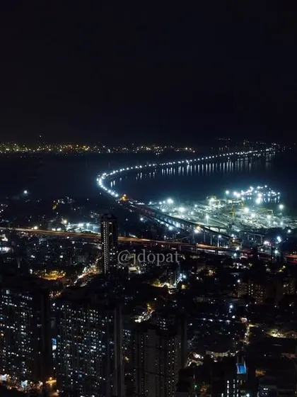 An aerial night view of Mumbai, showing the illuminated Trans Harbour Link stretching across the water.
