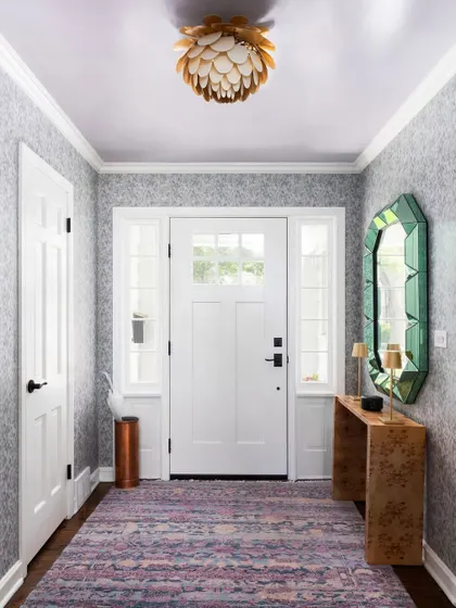 An entryway that makes a statement with patterned wallpaper and a unique, geometric mirror. The artistic ceiling light adds another layer of interest to this stylish entrance.