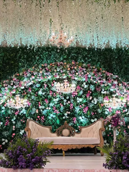 A breathtaking reception stage where a wall of lush greenery is densely packed with a variety of pastel flowers. This design creates the feel of an enchanted garden, complete with elegant candelabras and chandeliers.