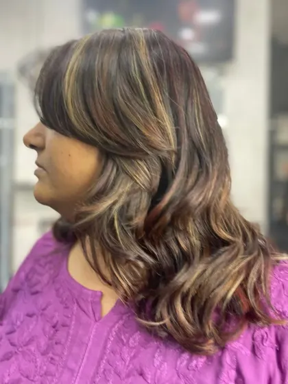 A side view of a layered haircut with bangs and soft waves. The highlights add depth and dimension to this chic, shoulder-length style.