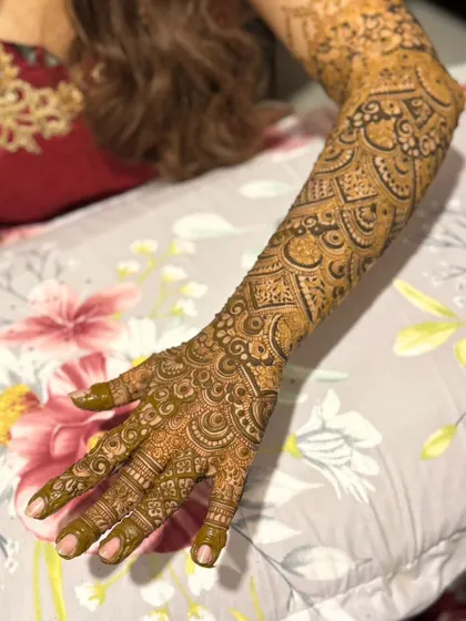 A full-arm bridal design shown resting on a pillow. The pattern is continuous and dense, a hallmark of traditional bridal mehendi.