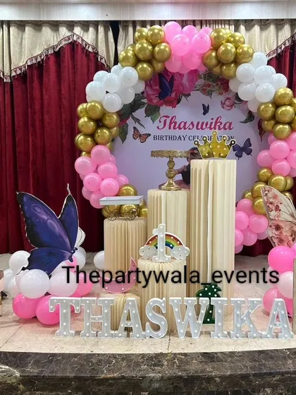 A pink and gold butterfly theme on a stage, with a large backdrop and picket fence.